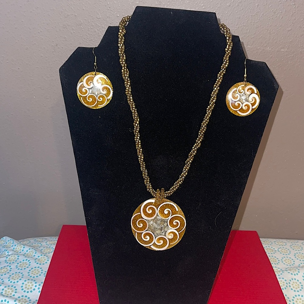 Gold beaded necklace with large pendant that has white spiral shell design